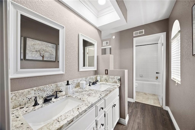 bathroom with baseboards, wood finished floors, toilet, double vanity, and a textured wall