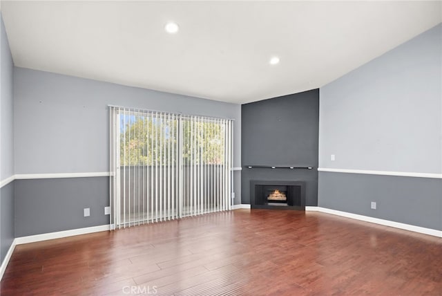 unfurnished living room with wood finished floors, baseboards, recessed lighting, and a lit fireplace