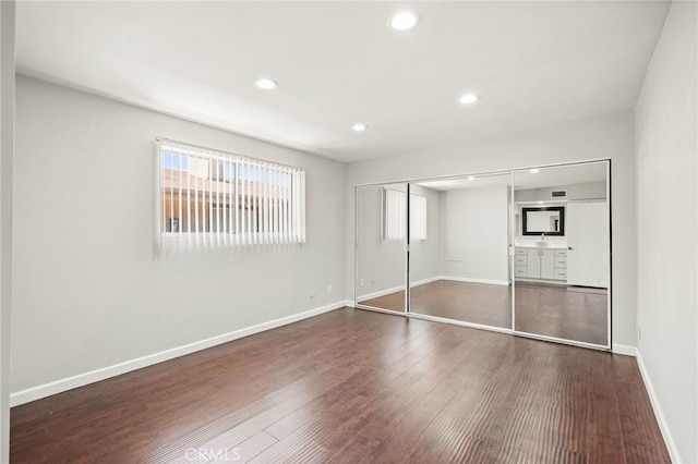 unfurnished bedroom featuring dark wood finished floors, recessed lighting, a closet, baseboards, and a sink