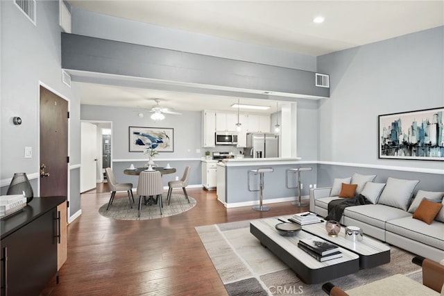 living room with dark wood-style flooring, a ceiling fan, and baseboards