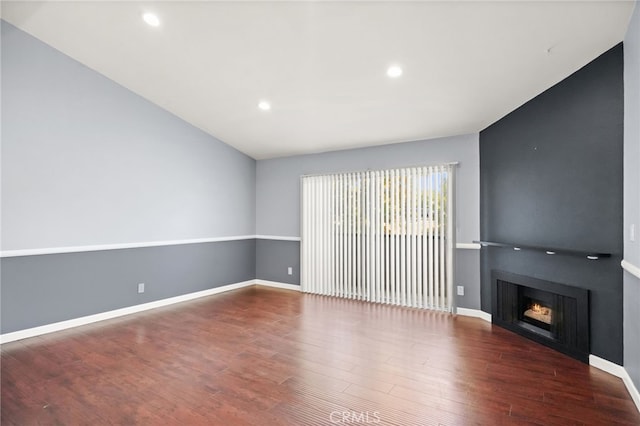 unfurnished living room featuring wood finished floors, a warm lit fireplace, recessed lighting, and baseboards