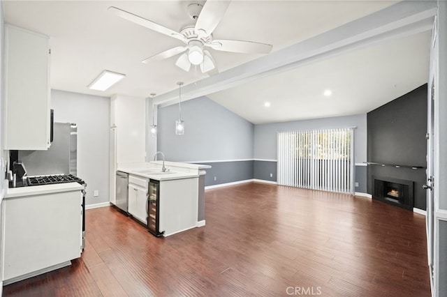 kitchen featuring appliances with stainless steel finishes, a sink, light countertops, a large fireplace, and a ceiling fan