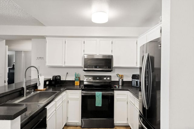 kitchen with appliances with stainless steel finishes, a sink, dark countertops, white cabinets, and a peninsula