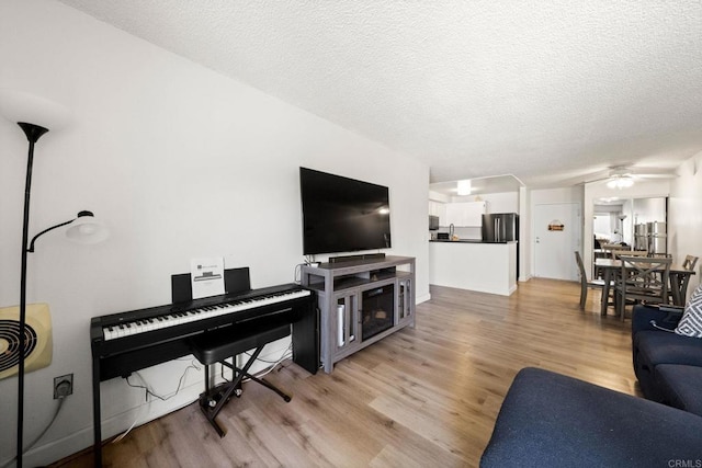 living area with light wood-style flooring, a textured ceiling, and a ceiling fan