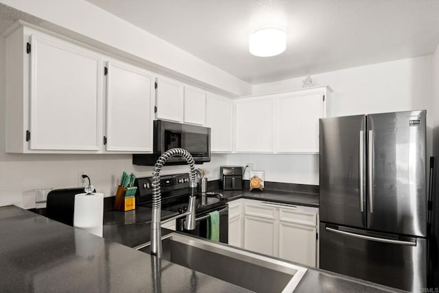 kitchen with freestanding refrigerator, dark countertops, electric stove, and white cabinetry
