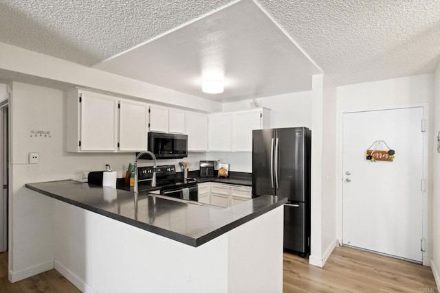 kitchen featuring freestanding refrigerator, electric range, a peninsula, dark countertops, and light wood finished floors