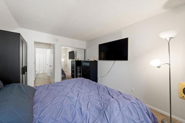 carpeted bedroom with a textured ceiling, baseboards, and ensuite bathroom