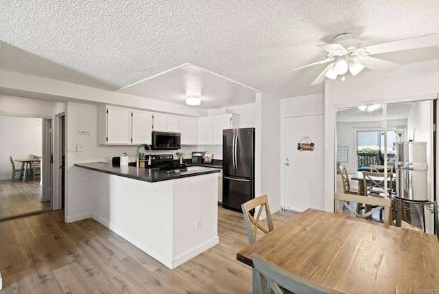 kitchen with freestanding refrigerator, a peninsula, dark countertops, a textured ceiling, and light wood-type flooring