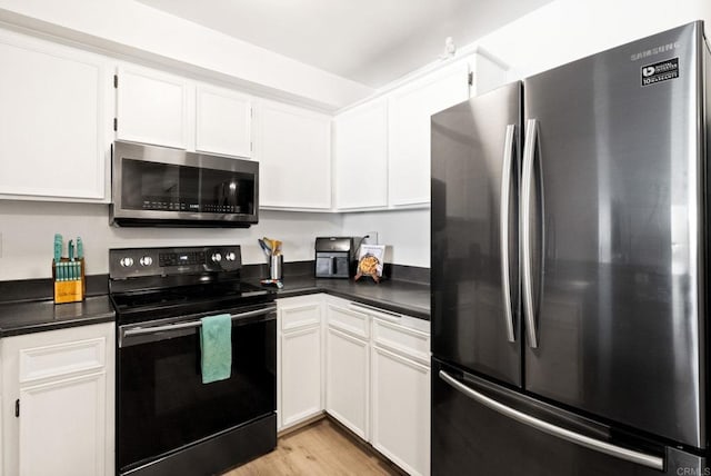 kitchen featuring stainless steel appliances, dark countertops, white cabinets, and light wood-type flooring