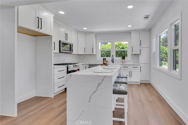 1925 N Marengo Ave, Pasadena, CA 91103 - kitchen with stainless steel appliances, decorative backsplash, light wood-type flooring, a kitchen breakfast bar, and light stone counters