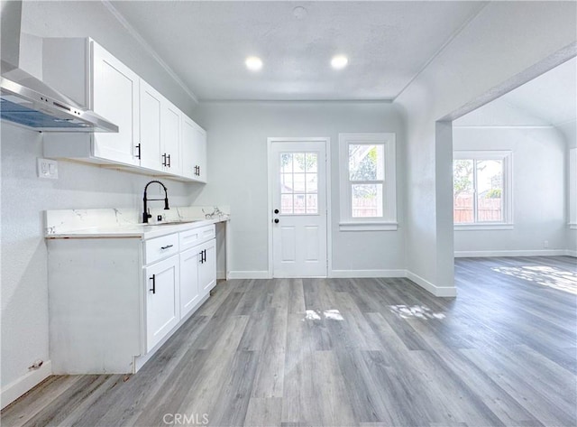 kitchen with wall chimney exhaust hood, light wood finished floors, baseboards, and light countertops