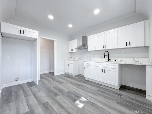 kitchen with wall chimney range hood, a sink, crown molding, white cabinets, and light countertops