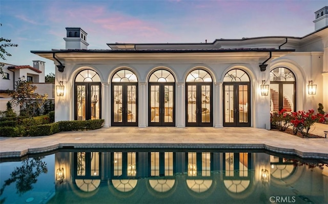 28 Shoreridge, Newport Coast, CA 92657 - back of house at dusk with french doors, an outdoor pool, a patio, and a chimney