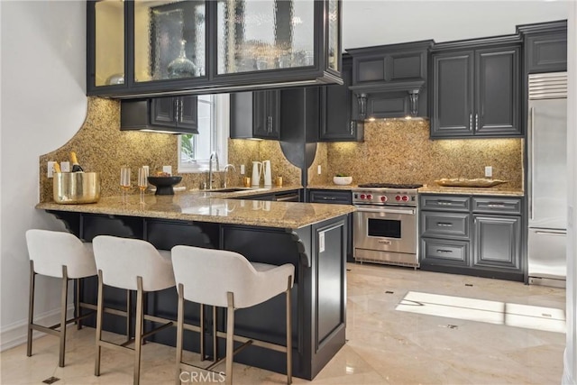 28 Shoreridge, Newport Coast, CA 92657 - kitchen with premium appliances, light stone countertops, a peninsula, a breakfast bar, and glass insert cabinets