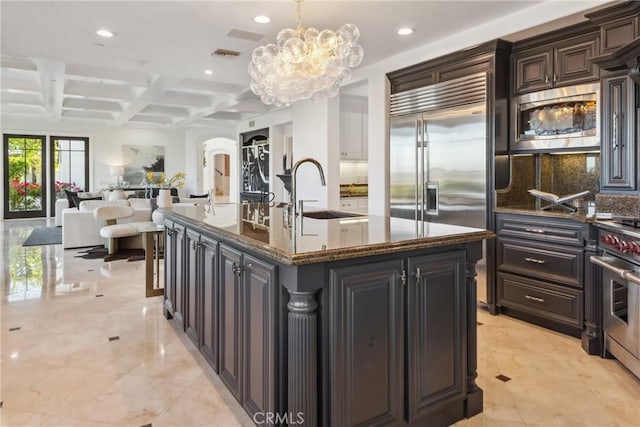 28 Shoreridge, Newport Coast, CA 92657 - kitchen with built in appliances, coffered ceiling, a chandelier, arched walkways, and an island with sink