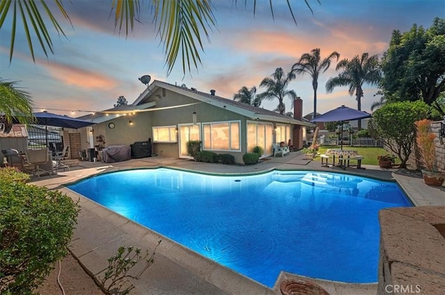 pool at dusk with a patio area and fence