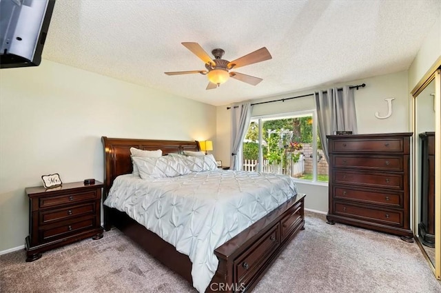 bedroom featuring light colored carpet, a textured ceiling, baseboards, and ceiling fan