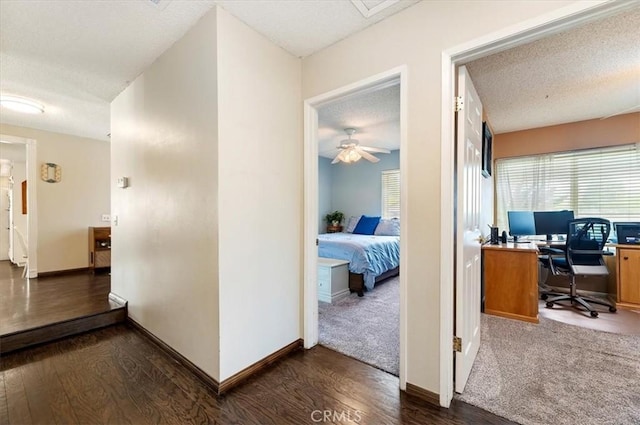 corridor featuring a textured ceiling, dark wood-style floors, a desk, plenty of natural light, and baseboards