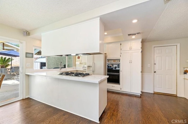 kitchen with stainless steel gas stovetop, a textured ceiling, dark wood finished floors, a peninsula, and white cabinets