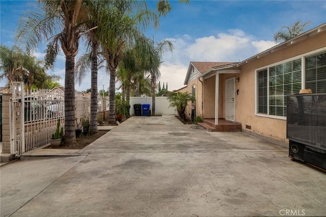 view of side of home with stucco siding, a gate, fence, and driveway