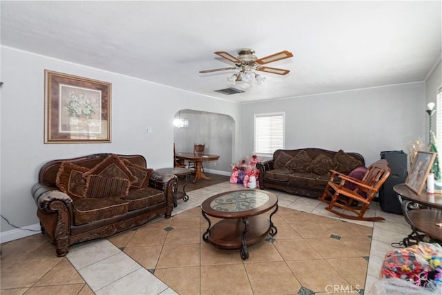 living area with arched walkways, light tile patterned floors, a ceiling fan, baseboards, and crown molding