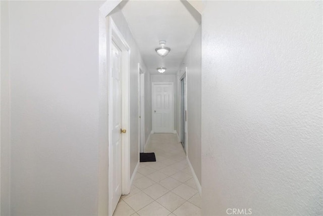 hallway with light tile patterned floors, baseboards, and a textured wall