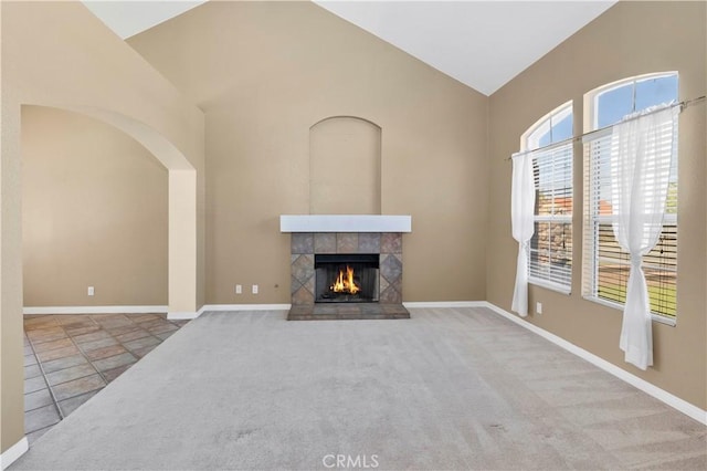unfurnished living room featuring high vaulted ceiling, carpet, a tiled fireplace, arched walkways, and baseboards