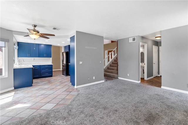 unfurnished living room with a ceiling fan, stairs, light carpet, and baseboards