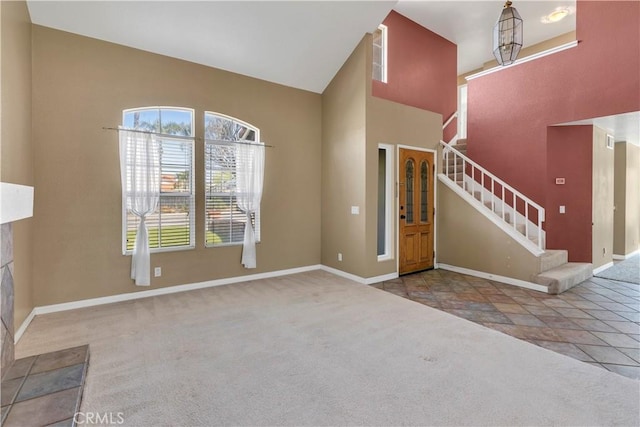 carpeted entrance foyer with stairway, baseboards, a high ceiling, and stone finish flooring