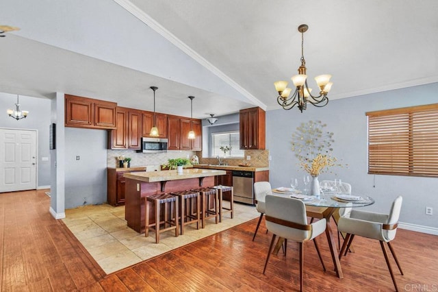 dining space featuring a chandelier, light wood-style flooring, vaulted ceiling, baseboards, and ornamental molding
