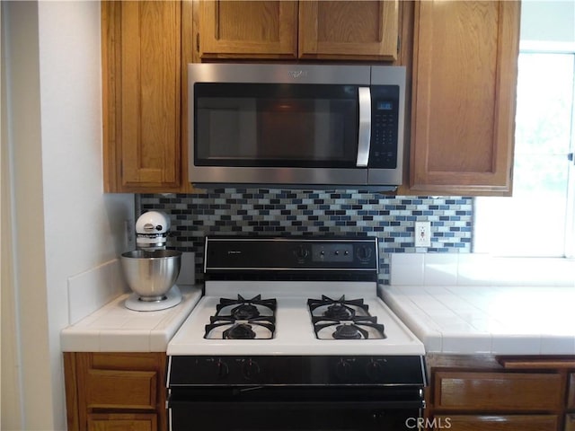 1806 Rory Ln Unit 9, Simi Valley, CA 93063 - kitchen with stainless steel microwave, gas stove, tile counters, decorative backsplash, and brown cabinets