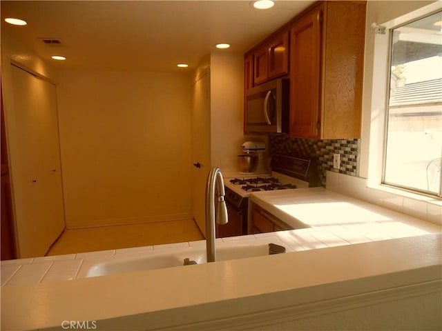 1806 Rory Ln Unit 9, Simi Valley, CA 93063 - kitchen featuring stainless steel microwave, white gas stove, brown cabinetry, tasteful backsplash, and recessed lighting