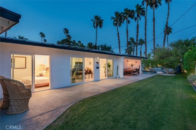 back of house with stucco siding, a patio area, and a yard