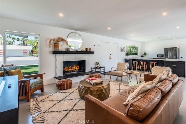 living area with finished concrete flooring, a brick fireplace, and recessed lighting