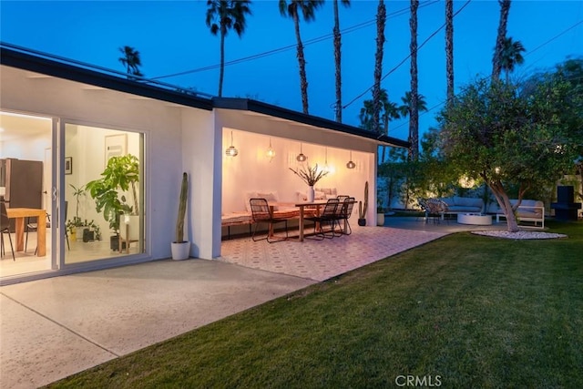 rear view of house with an outdoor hangout area, a patio, stucco siding, and a lawn