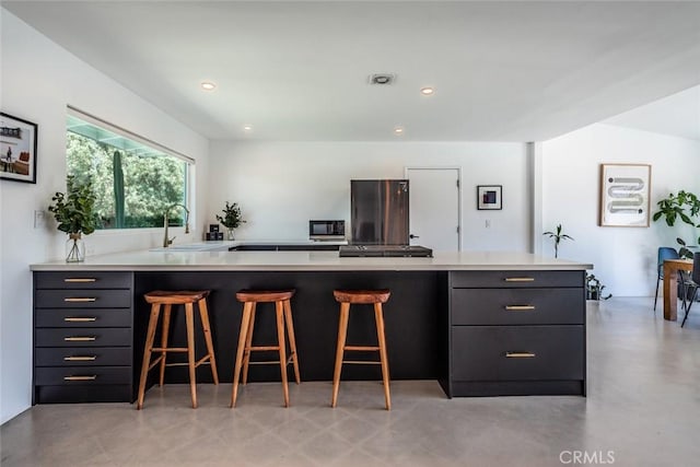kitchen with a sink, light countertops, a kitchen bar, modern cabinets, and recessed lighting