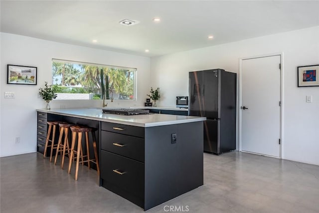 kitchen with freestanding refrigerator, dark cabinets, a kitchen breakfast bar, light countertops, and a peninsula
