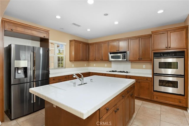 kitchen featuring stainless steel appliances, brown cabinetry, a center island with sink, light tile patterned floors, and recessed lighting