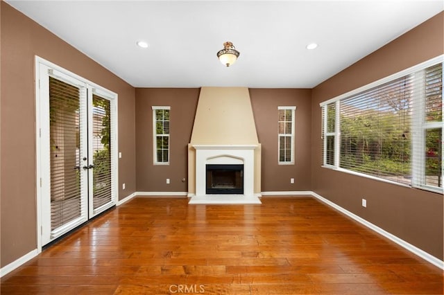 unfurnished living room featuring wood-type flooring, baseboards, a fireplace, recessed lighting, and french doors