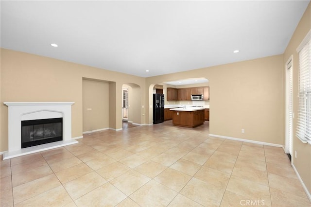 unfurnished living room with arched walkways, light tile patterned flooring, recessed lighting, a glass covered fireplace, and baseboards