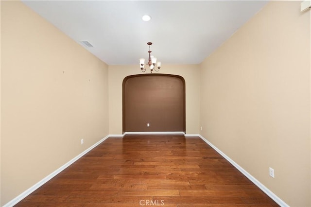 unfurnished dining area with a chandelier, arched walkways, wood finished floors, baseboards, and recessed lighting