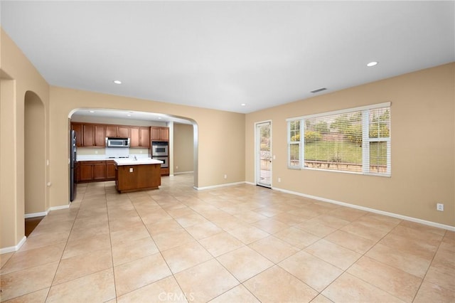 unfurnished living room featuring arched walkways, light tile patterned floors, recessed lighting, and baseboards