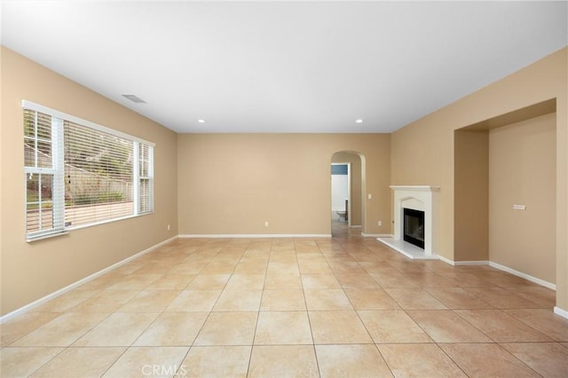 unfurnished living room with arched walkways, light tile patterned floors, a glass covered fireplace, recessed lighting, and baseboards