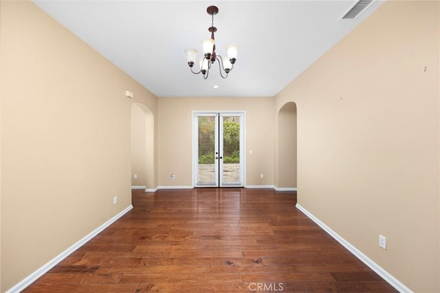 empty room with arched walkways, a chandelier, baseboards, and wood finished floors