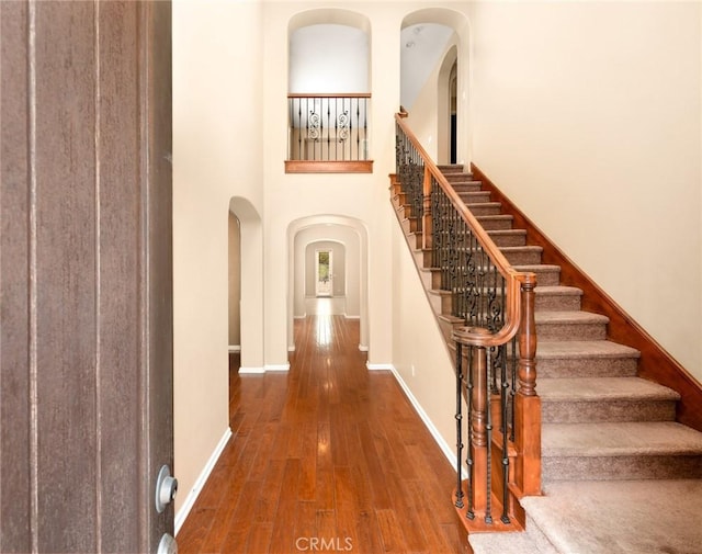 entryway with arched walkways, wood finished floors, stairway, baseboards, and a high ceiling