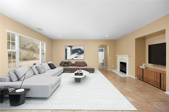 living area featuring arched walkways, light tile patterned flooring, recessed lighting, a glass covered fireplace, and baseboards