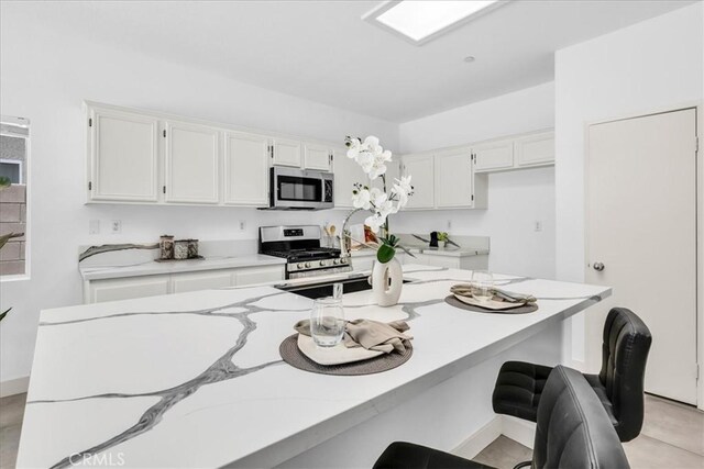3773 Mission, Peak, Palm Springs, CA 92262 - kitchen with stainless steel appliances, white cabinets, a breakfast bar area, baseboards, and light stone counters