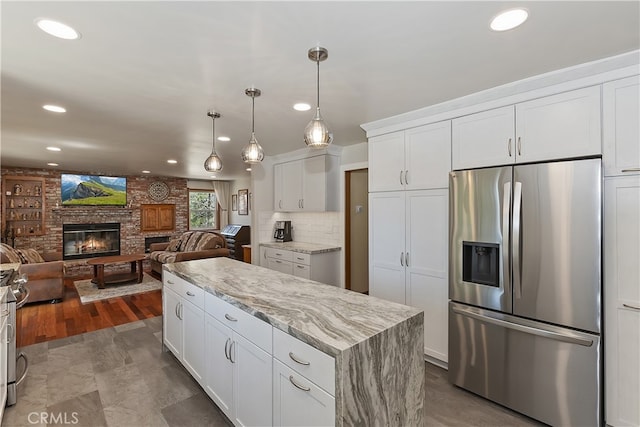 27513 St Bernard Ln, Lake Arrowhead, CA 92352 - kitchen with stainless steel fridge with ice dispenser, a kitchen island, a brick fireplace, white cabinetry, and light stone countertops