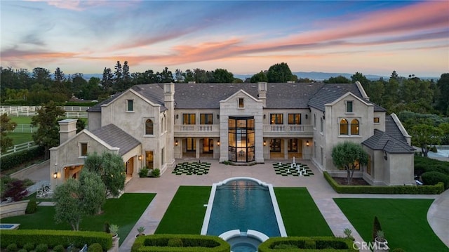 18 Dovetail Ln, Bradbury, CA 91008 - back of house at dusk featuring a balcony, a patio area, stone siding, a pool with connected hot tub, and stucco siding