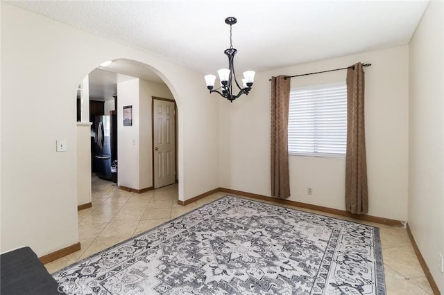 unfurnished room with arched walkways, a chandelier, light tile patterned floors, and baseboards